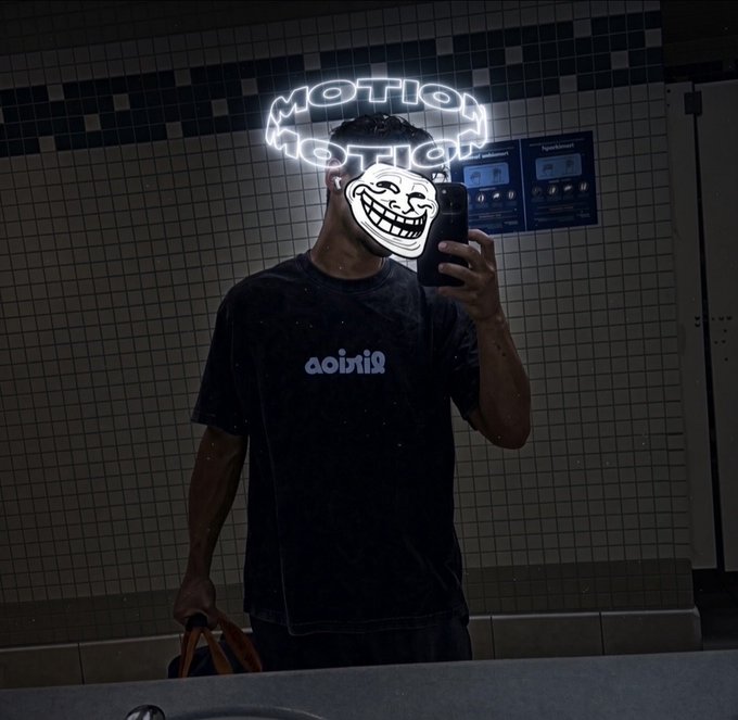 A mirror selfie of a person wearing a black 'aditxiS' t-shirt, with a glowing neon 'MOTION' sign and a troll face meme overlay covering their face.