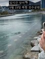 The photo captures a coastal shoreline with text overlay reading "당신은 왜냐? 이 사내 말에 5배는 쳐야죠" (roughly: "Why? You should multiply that man's words by 5"). The accompanying post references a "Busan Shark Teacher," suggesting the image relates to a viral clip of a fishing authority in Busan advising viewers to significantly amplify (5x) his words, likely about shark sightings or beach safety, with the rocky shoreline and murky water hinting at the local coastal setting.