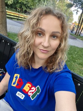 The image shows a woman sitting on a park bench, wearing a blue shirt with colorful letters. The photo appears to be taken at a specific moment when she's posing for a picture. There are no visible texts or additional objects in the scene that would help determine the content of the post.