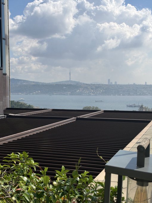A scenic view from a rooftop terrace overlooking a body of water with a city skyline and a prominent tower in the distance, under a partly cloudy sky. The image sets a reflective morning mood that complements the post's theme of reassessing strategy after $BONK and $INJ trades, suggesting a fresh start.