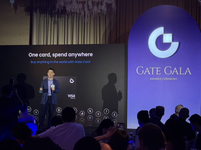 A man in a suit delivers a presentation at the "Gate Gala Awards Ceremony," standing beside a screen promoting "One card, spend anywhere" with the tagline "Buy anything in the world with Gate Card," featuring a Visa logo. The image illustrates the post's point about Gate's boss joining other exchange executives in confidently giving English speeches on stage.