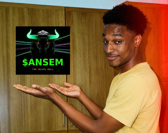 A young man in a yellow t-shirt gestures toward a poster on a wooden cabinet that displays a glowing green bull graphic with the text '$ANSEM THE BLACK BULL'.