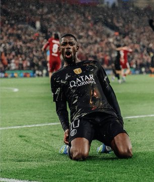 A soccer player wearing a black Paris Saint-Germain (PSG) kit with "QATAR AIRWAYS" sponsorship is seen kneeling and celebrating passionately on the pitch.