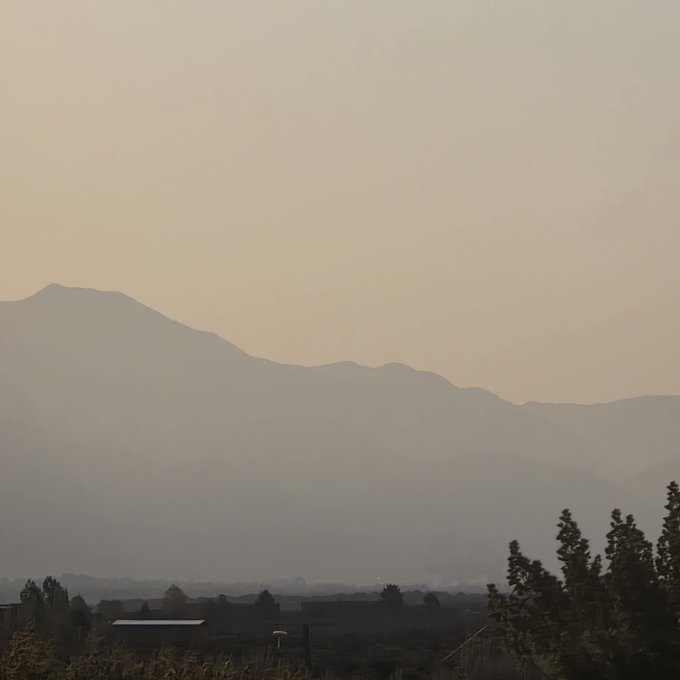 A hazy, sunset landscape photograph showing silhouetted mountains in the distance above a dark valley.