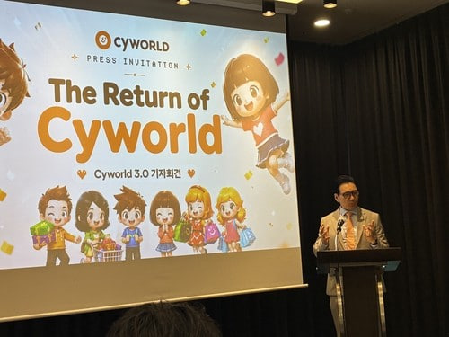 A man speaking at a podium during the Cyworld press event 'The Return of Cyworld,' with a presentation slide announcing Cyworld 3.0 and showing cartoon character avatars.