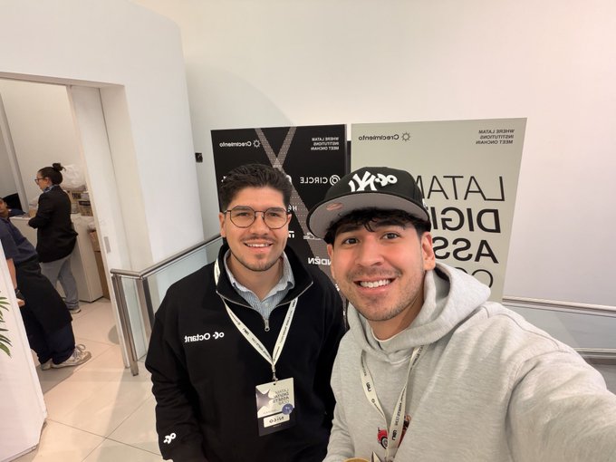Two men smiling for a selfie at an event, wearing lanyards with 'Circumference' and 'LATAM RISE ARGENTINA' branding visible on signage behind them.