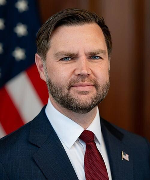A formal portrait of U.S. Vice President JD Vance in a dark suit and red tie, standing before an American flag.