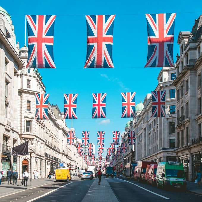 British Union Jack flags strung across a bustling London street with "ZARA HOME" visible on a storefront, setting a patriotic scene appropriate for news about the UK's first digital-native government bond pilot led by major banks including Barclays, HSBC, and Lloyds.