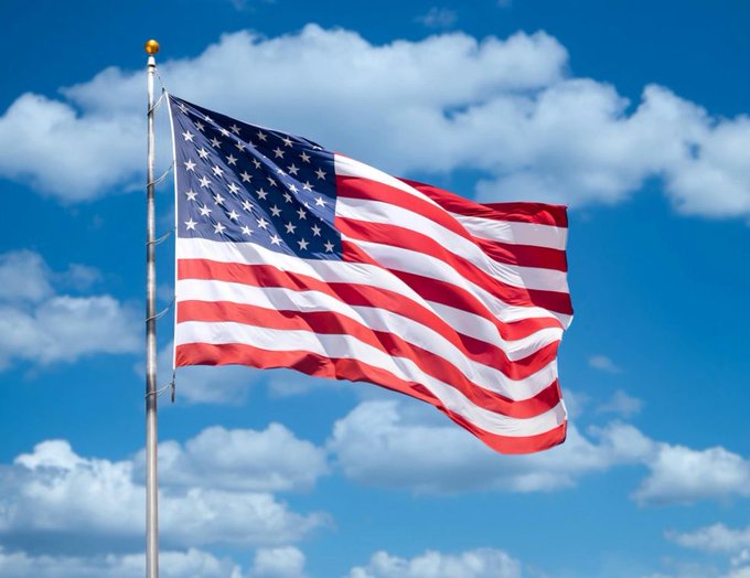 An American flag waves in the wind against a bright blue sky dotted with white clouds.