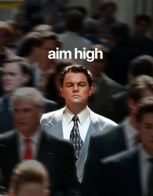 Leonardo DiCaprio as Jordan Belfort from 'The Wolf of Wall Street' standing still in a crowd, overlaid with the text 'aim high'.