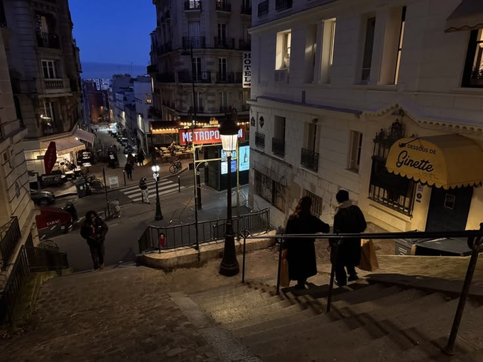 The image shows a couple walking up a flight of stairs at night, with a building nearby that has a sign for "metro toussainte" above it. The scene appears to be set in Paris, as suggested by the presence of a street lamp and other city elements such as cars parked on the street and people walking around. The image also includes text that reads "goodnight lads exciting stuffs @sleepagotchi tomorrow $SLEEP is coming".