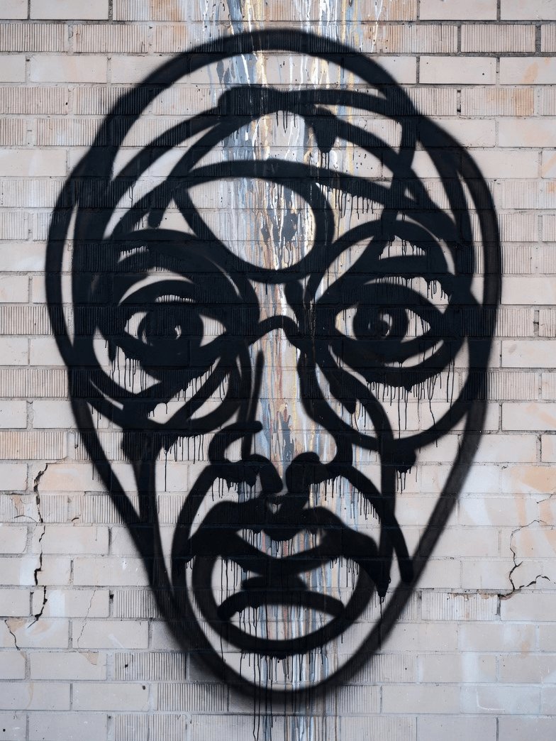 The image features a black and white graffiti of a face, possibly a mask or a sculpture, set against a brick wall backdrop. The text "Masks are coming" is written above the image, which could be interpreted as a warning about masks being drawn on the wall. This message might be related to an event or situation where masks have been drawn in public spaces, such as protests or gatherings.