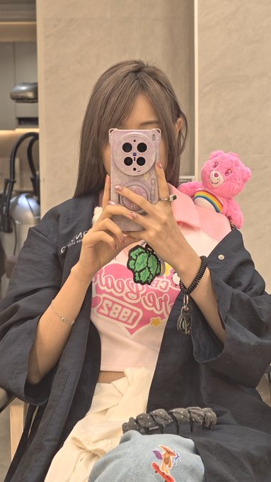 A young woman takes a mirror selfie wearing a dark "Calvin Klein" jacket over a white graphic tee, accompanied by a pink Care Bear plush. The image relates to the post "今天过后 我将正式告别黄毛" (Today after, I will officially say goodbye to yellow hair), suggesting a farewell to her previous blonde look as her hair now appears to be transitioning to a darker tone.