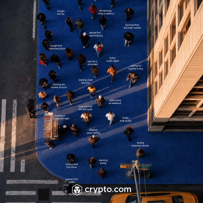 An aerial view of pedestrians crossing a blue-painted street, each labeled with a milestone in their crypto investing journey — from "bought first btc" to "survived their first bear market" — with the Crypto.com logo and a yellow taxi visible below. The ad plays on the viewer identifying with a specific stage, while the post narrows it down: "First buy, fifth cycle, somewhere in between. Which one are you?"