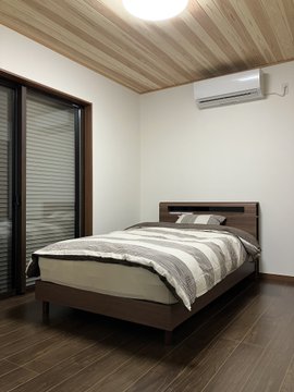A minimalist bedroom with a wooden bed, white bedding, a wall-mounted air conditioner, wood-paneled ceiling, and dark wood flooring.