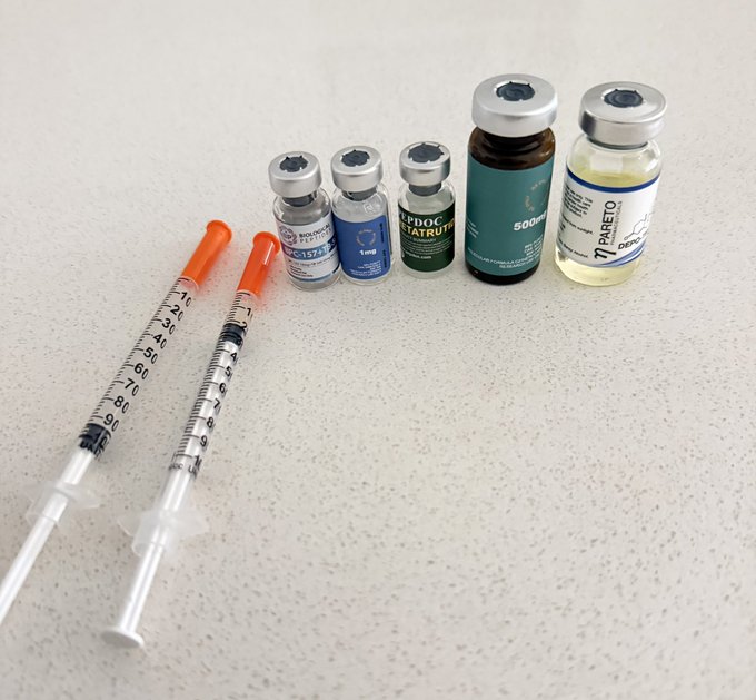 Two insulin syringes lie next to four vials of research peptides, with visible labels reading "BPC-157," "1mg," "PIPOTRASTATROL," "500mg," and "Pareto," illustrating the user's reference to buying and using $PEPTIDES.
