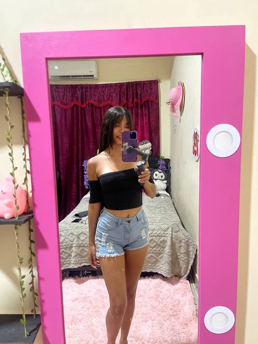 A woman takes a mirror selfie in her bedroom, which features a large pink-framed mirror, maroon curtains, and a plush teddy bear on the bed. The caption "Do you really think I can find something?" suggests she's searching her closet or room for an outfit, possibly expressing doubt about finding something to wear.