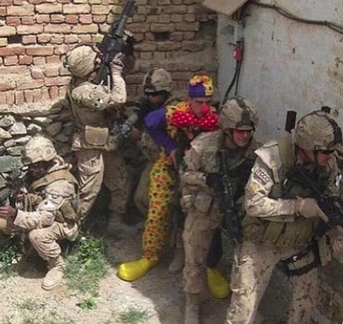 A clown in a colorful polka-dot and star-patterned outfit stands surrounded by heavily armed soldiers in camouflage gear and helmets within a narrow alleyway. The image humorously juxtaposes the absurdity of a brightly dressed clown appearing in a tense military setting, mirroring the post's ironic commentary on the $BEM token holders' chat where supposedly brilliant individuals are likely just joking around rather than discussing anything serious.