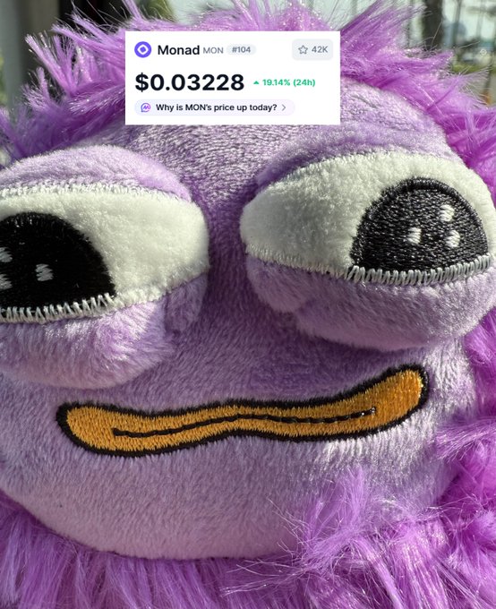 A close-up of a fluffy purple monster plush toy with half-closed eyes and a yellow smile, with a crypto price ticker showing "Monad MON #104" at $0.03228, up 19.14% in 24 hours.