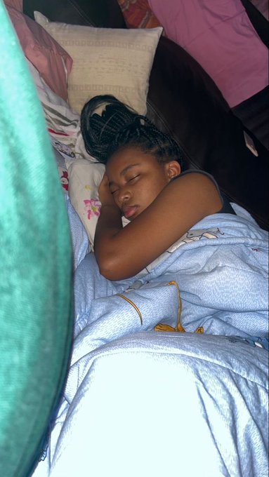 A young girl with braided hair peacefully sleeping in bed under a blue blanket with a green fabric in the foreground.