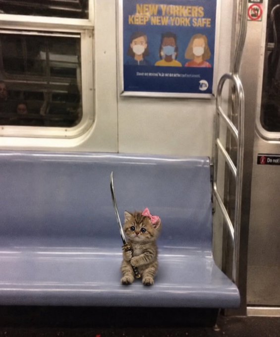 A small tabby kitten with a pink bow sits on a subway seat holding a tiny sword, beneath an MTA poster reading 'NEW YORKERS KEEP NEW YORK SAFE'.