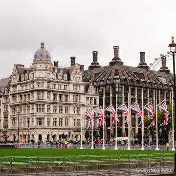 A view of London features classical buildings with a domed roof and British Union Jack flags lining the street in the foreground.