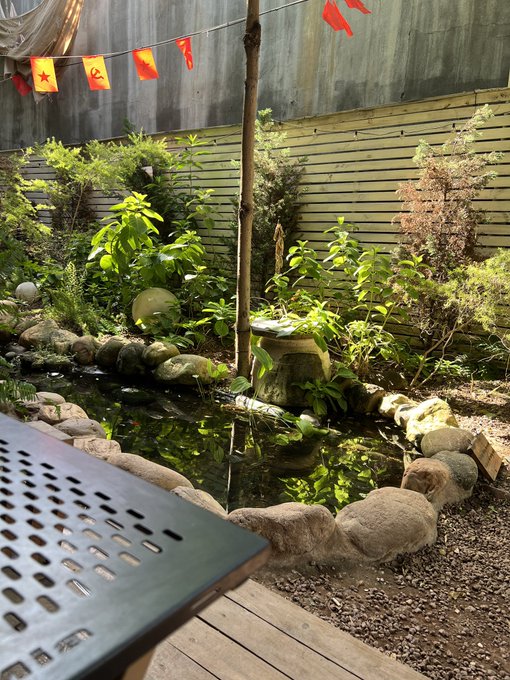 A small garden pond surrounded by rocks, plants, and bamboo, decorated with Vietnamese flags strung across the top and featuring a traditional water feature.
