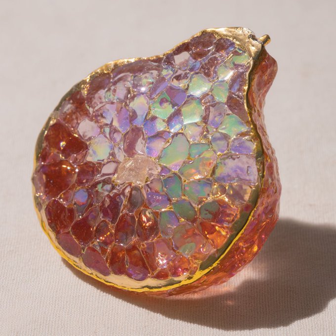A decorative apple-shaped object covered in iridescent pink, purple, and orange crystal pieces with gold accents, displayed on a light surface.