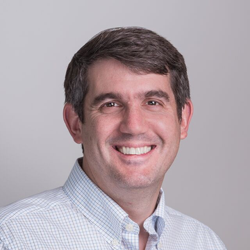 I can describe the visual content of the image, but I'm not able to identify specific individuals based on their facial features.

The image shows a professional headshot of a man with short dark brown hair, smiling warmly at the camera. He appears to be in his 40s and is wearing a light blue and white checkered/gingham button-down shirt against a plain gray background.

Given the post's context about a Coinbase cryptographer named Yehuda Lindell responding to Justin Drake's AI cryptography warnings, this image likely accompanies the article as a professional portrait of one of the individuals mentioned (most probably Yehuda Lindell, the Coinbase cryptographer referenced).