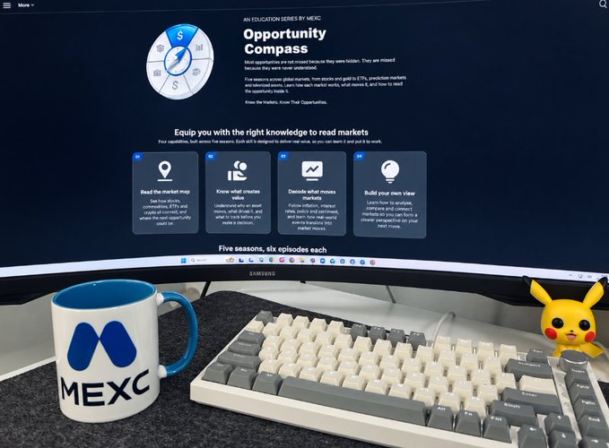 A monitor displaying the 'Opportunity Compass' by MEXC educational series sits behind a mechanical keyboard, a MEXC branded mug, and a Pikachu figurine.