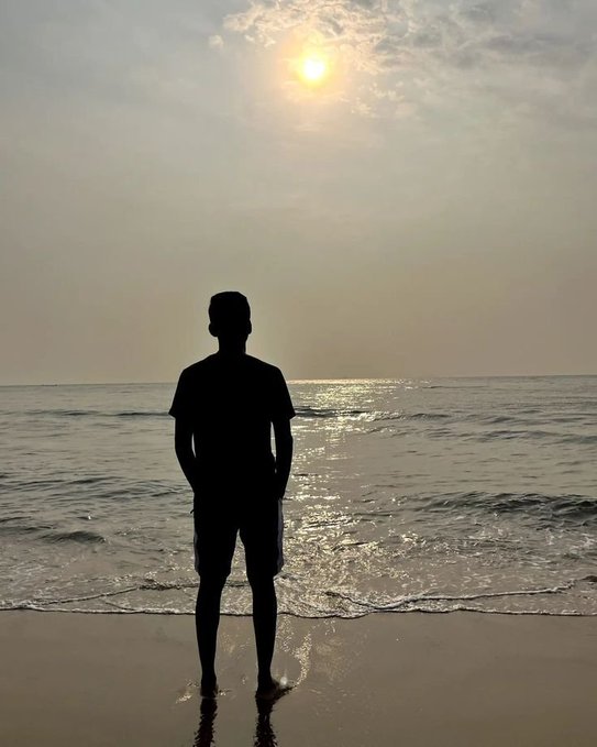 A silhouette of a person standing on a beach facing the ocean at sunset.