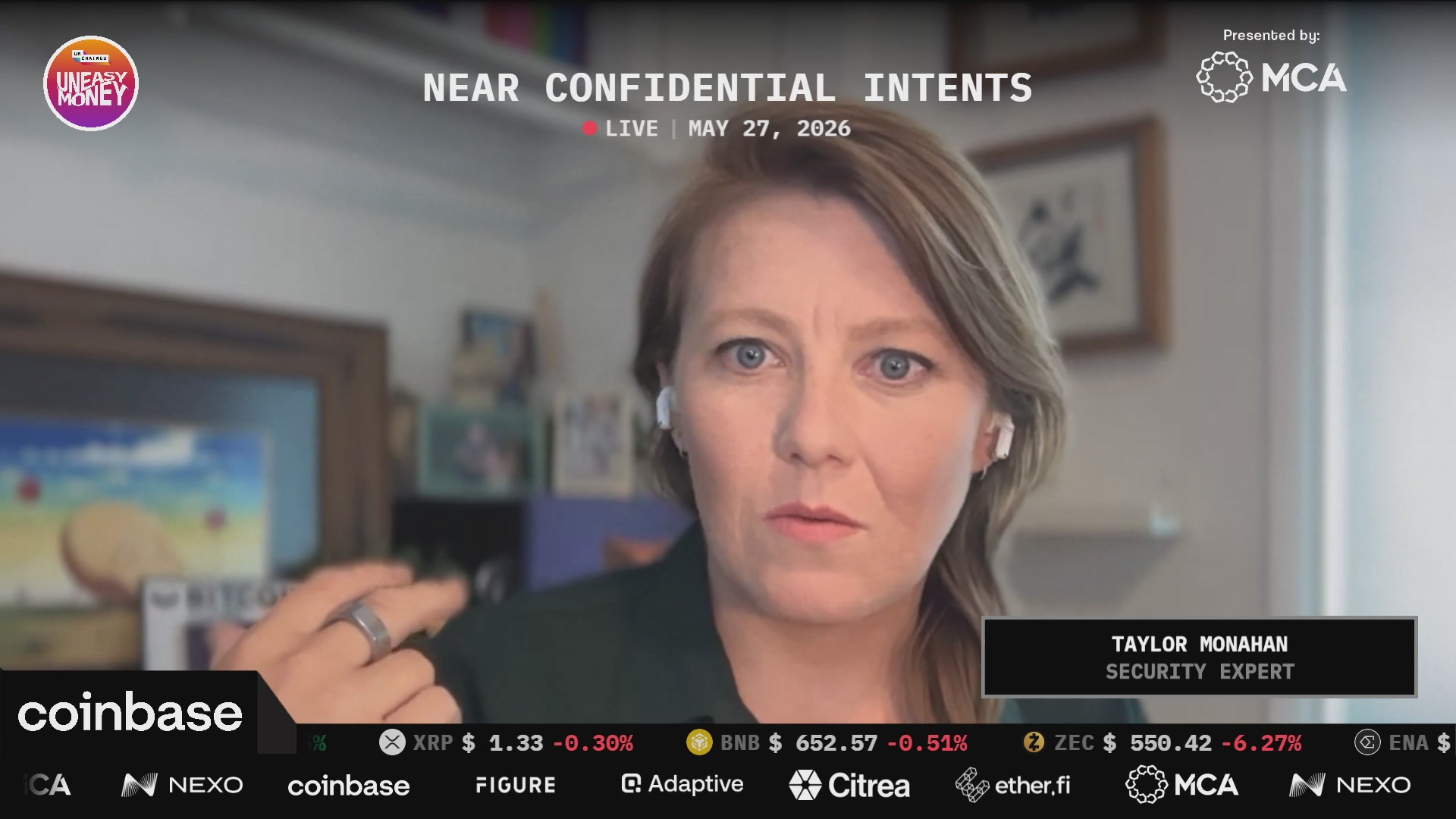 The image shows a woman wearing earbuds with a microphone attached to her face while sitting at a desk or table. The background of the image features a TV screen displaying a computer monitor, suggesting that she might be participating in an online meeting or conference call. The text on the screen reads "Near Confidential Intentions Live 7/27/2020", indicating that there is a scheduled event for the woman to attend.