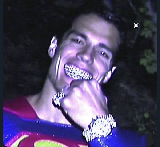 A purple-tinted photo of a man smiling with a large, sparkling diamond-encrusted watch and matching grill on his teeth.