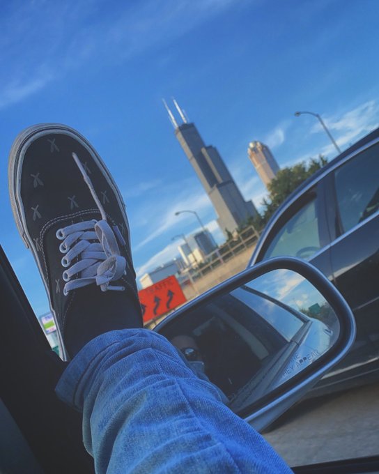 A person rests their sneaker-clad foot out a car window, with Chicago's Willis Tower visible in the background under a bright blue sky. The image perfectly captures the "breathtaking view" of the workweek ahead from a comfortable distance, embodying the casual Wednesday escape the post describes.
