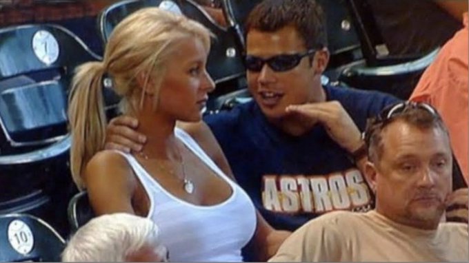 A couple sits in stadium seats, with the man’s shirt reading “ASTROS” and nearby seats showing numbers 9 and 10. The post’s discussion of perpetual markets over continuously changing information fits the image’s “always on” sports-event atmosphere, where events and commentary keep unfolding.