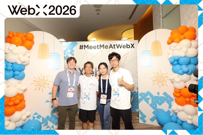 A photo of four people posing together at a WebX 2026 event with a '#MeetMeAtWebX' backdrop and orange and blue balloon decorations.