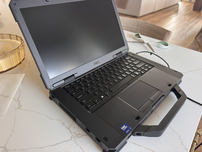 A rugged black Dell rugged laptop (Latitude model) sitting open on a white marble countertop with a built-in carrying handle visible on the right side.