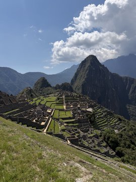 A scenic view of Machu Picchu, featuring the ancient stone ruins and terraces nestled among green mountains under a partly cloudy sky.