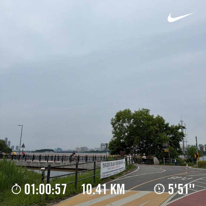 The image shows a person running along a street, as indicated by the text "Anoma run #Anomarun @ Cryptowombat125". The runner appears to be wearing athletic shoes while going for a jog. The road they are running on is part of a larger urban landscape that includes a bridge and buildings in the background. This photo may be related to an app or website showcasing their running achievements, such as tracking distance, time, or other fitness data during their runs.