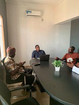 Three people sit around a black conference table in a meeting room with a wall-mounted air conditioner, with a small potted plant in the center of the table and a laptop open in front of the woman on the right. The image captures the in-person gathering referenced in the post, showing the attendees—including those tagged as @240Nature, @InvestorUsman, @web3osamah, and Mujaheed—meeting together.