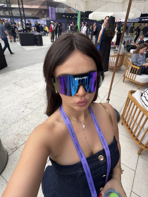 The image features a woman wearing blue jeans, purple sunglasses, and holding a green ball. She appears to be posing for a photo or selfie. The caption of the image reads "top 5 horror movies: 1. doesn't do crypto 2. thinks arrogance is a personality trait 3. isn't a solana maxi 4. doesn't trench". This suggests that she might have recently watched one of these five horror movies, and she wants to share her thoughts on them with others through the photo or selfie.