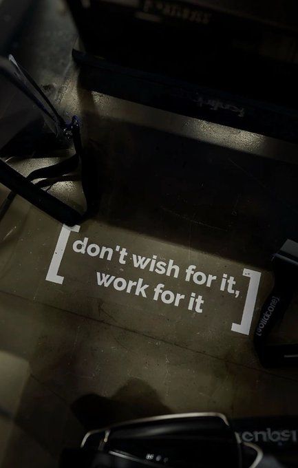 iced coffee and a black suitcase are present on the floor, with a motivational quote "Don't wish for it, work for it" displayed above them.