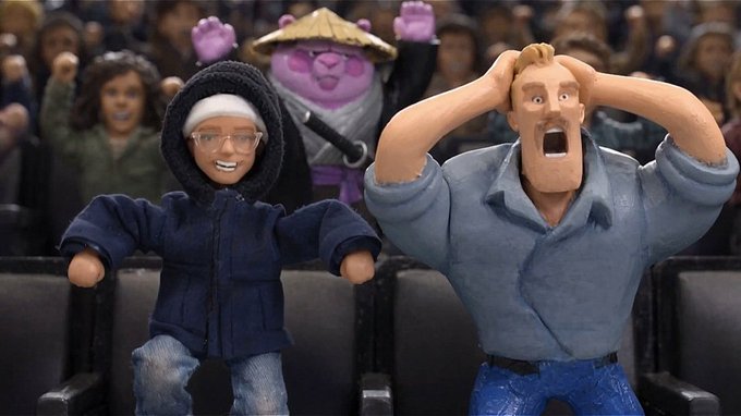 Claymation-style scene of audience figures at what appears to be a movie theater, featuring a woman in a blue hooded jacket smiling next to a shocked man in a blue shirt with hands on his head, with a purple character wearing a straw hat visible in the background.