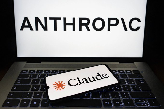 A smartphone displaying the 'Claude' logo rests on a laptop keyboard, with the word 'ANTHROPIC' shown on the laptop screen in the background.