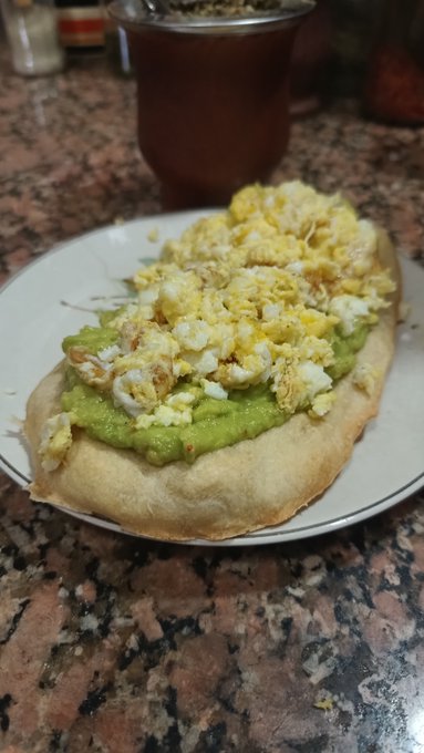 A plate of food on a granite counter appears to be an arepa or flatbread topped with green guacamole and a generous portion of scrambled eggs.
