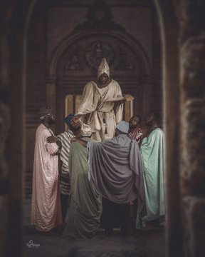 A fantasy illustration of a hooded figure in white robes standing elevated before several other robed figures in an ornate stone chamber.