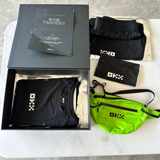 A black OKX Mid-Autumn Festival gift box contains a matching set of branded apparel and accessories, including a black athletic shirt, black shorts, a black waist pouch, and a neon green crossbody bag, all displayed alongside a festive greeting card. The image illustrates the Mid-Autumn Festival merchandise haul mentioned in the post, which expresses appreciation for receiving the coordinated OKX activewear set.