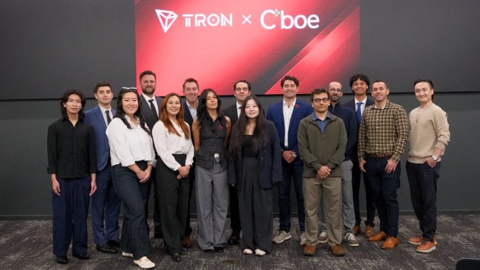 A group photo of approximately fifteen people in business attire standing in front of a screen displaying the logos "TRON x Cboe".