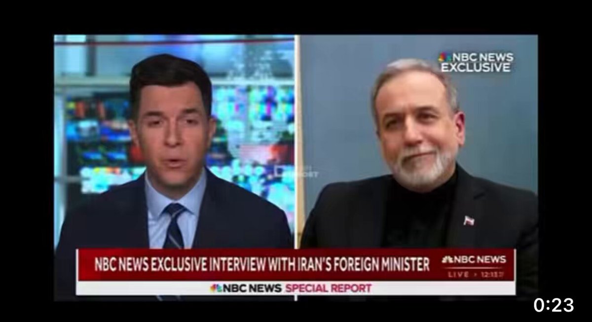 The image shows two men sitting across from each other at a news desk with a TV screen displaying them. The man on the left side of the image has his mouth open, while the man on the right side appears to be speaking or listening attentively. They are both wearing suits and ties, suggesting that they might be discussing an important topic related to politics or international relations.