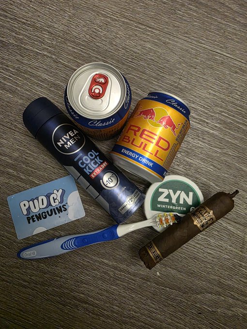 Photo showing a PUDGY PENGUINS card, Nivea Men Cool Kick deodorant, Red Bull energy drink, Oral-B toothbrush, ZYN Wintergreen nicotine pouch, and a cigar arranged on a wooden surface.